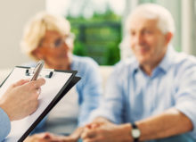 Senior couple having meeting with financial advisor or insurance agent. Close up of female hand holding pen and clipboard.