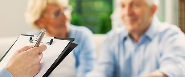 Senior couple having meeting with financial advisor or insurance agent. Close up of female hand holding pen and clipboard.