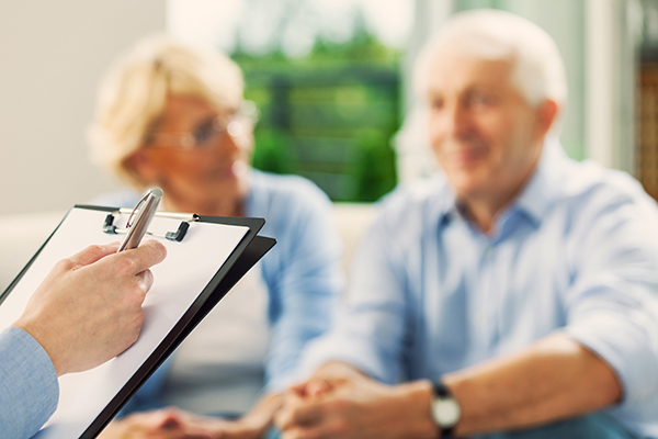 Senior couple having meeting with financial advisor or insurance agent. Close up of female hand holding pen and clipboard.